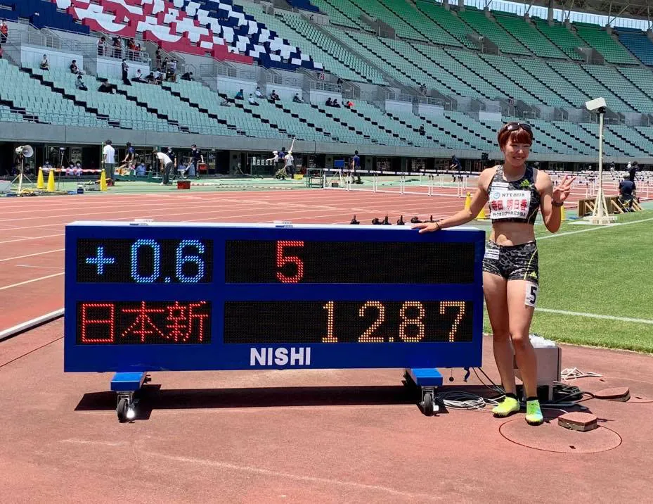 日本新記録12秒87の記録表示板の隣に立つ寺田明日香
